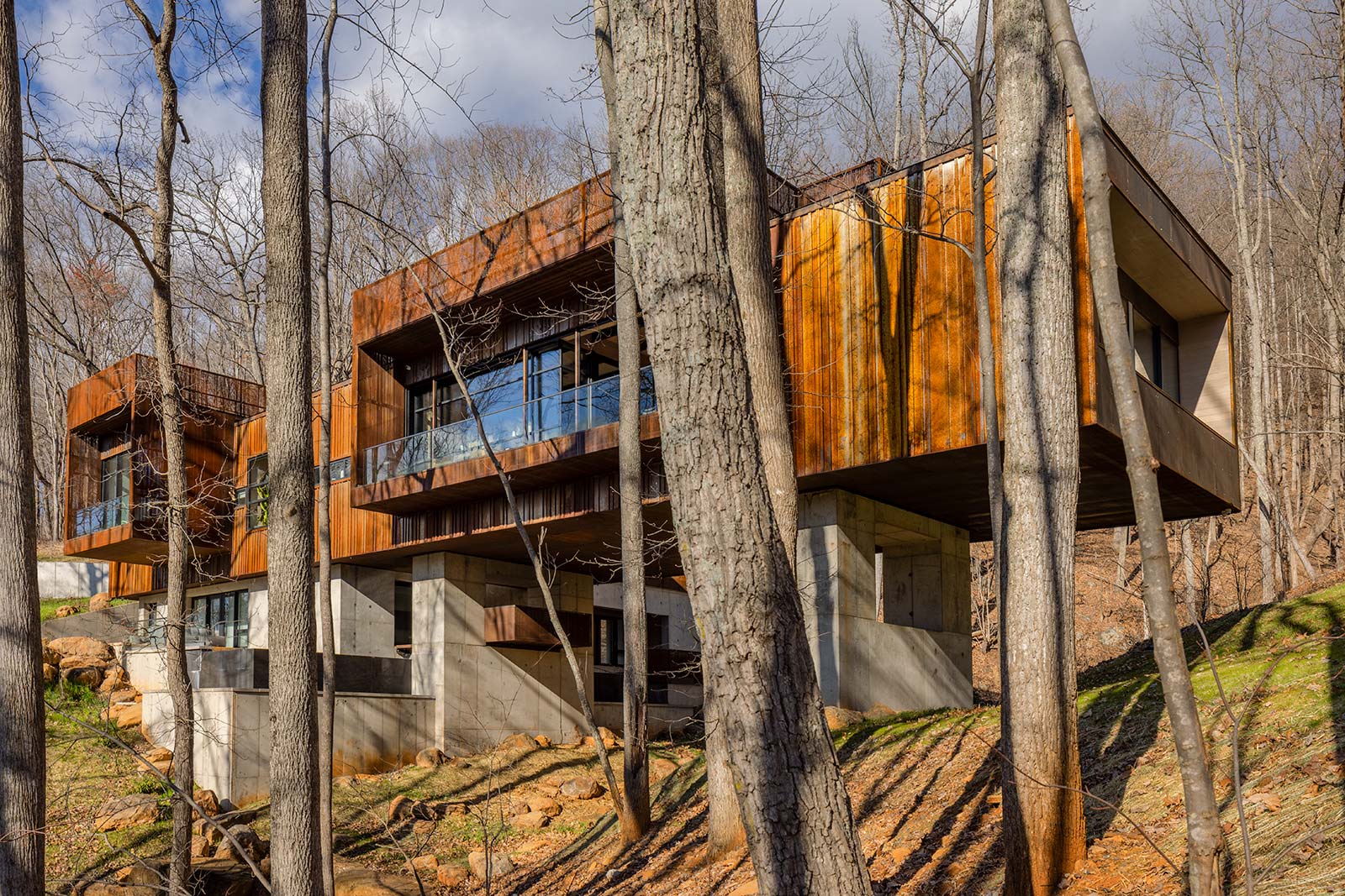 View of Corten Rusted Steel Perforated Screens and Ribbed Metal Siding at Modern Bridge House Spanning Ravine on Concrete Piers by Best Charlottesville Architects HEDS Designed by Allison Ewing.