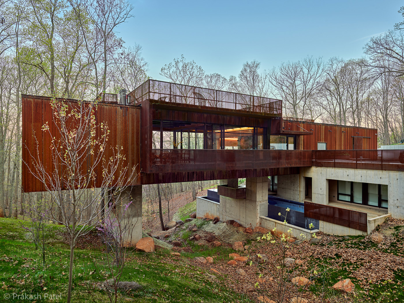 View of Corten Rusted Steel Perforated Screens and Ribbed Metal Siding at Modern Bridge House Spanning Ravine on Concrete Piers by Best Charlottesville Architects HEDS Designed by Allison Ewing.